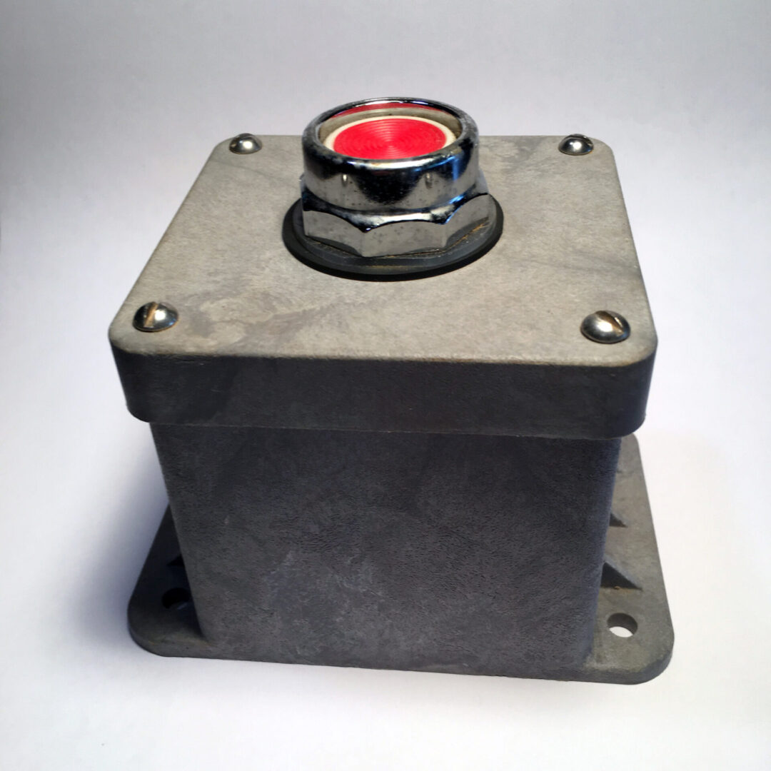 A square metal box with a red button on top.